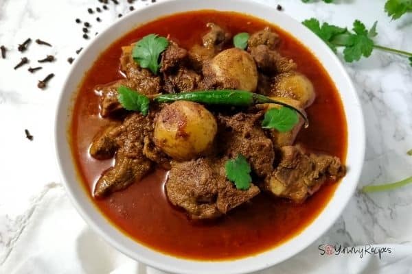 ready made Aloo Gosht - the meat and potato curry in a white bowl with spices and coriander leaves around