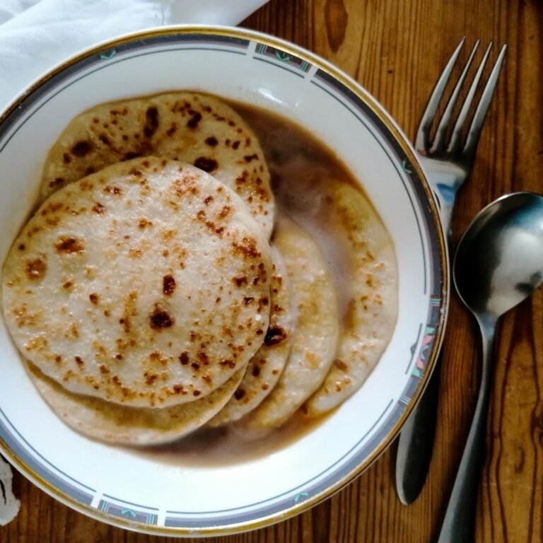 A bowl of Indonesian pancakes with brown sugar syrup and coconut milk with spoon and fork