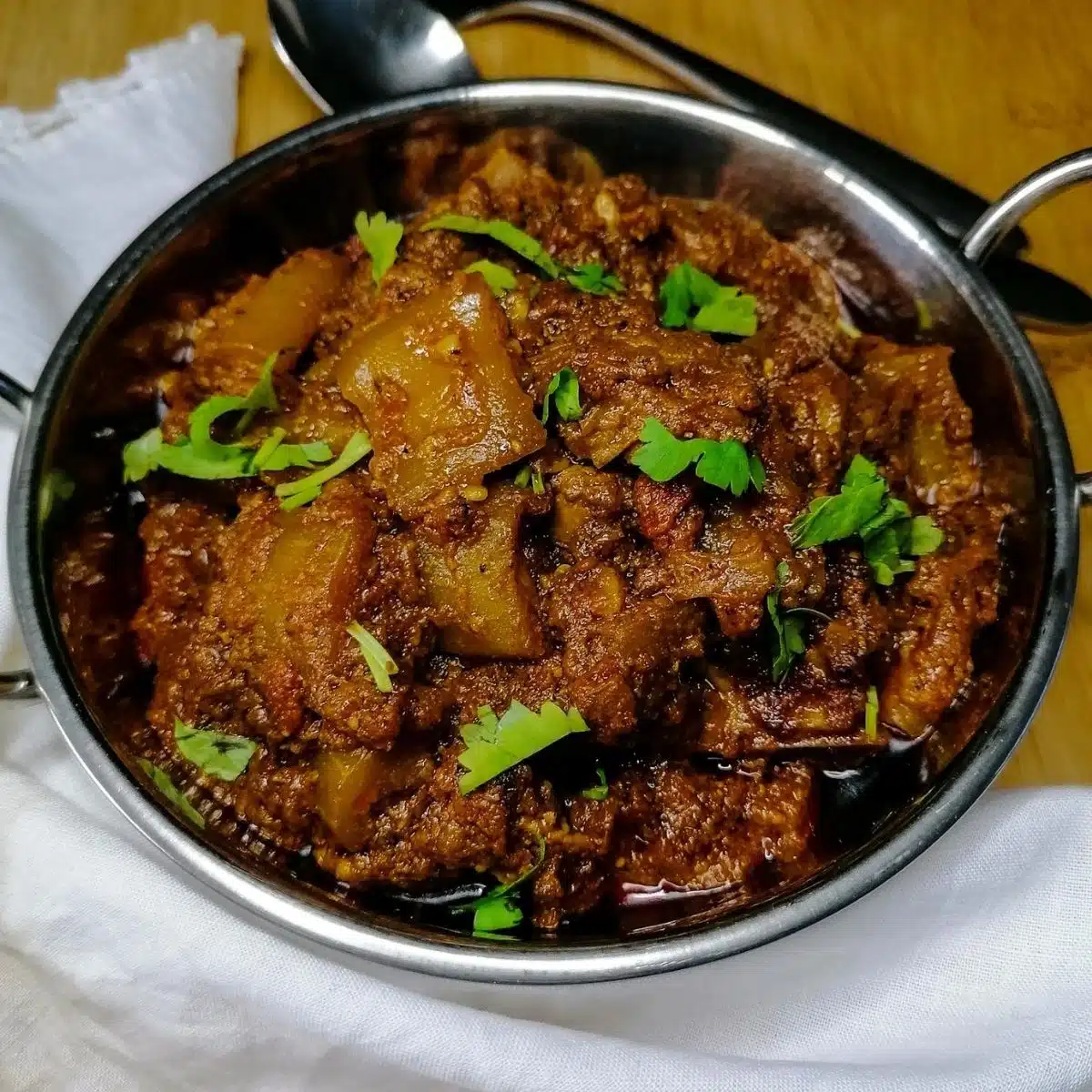 Pakistani Lauki gosht - meat and bottle gourd curry in a stainless steel serving bow with spoon and fork