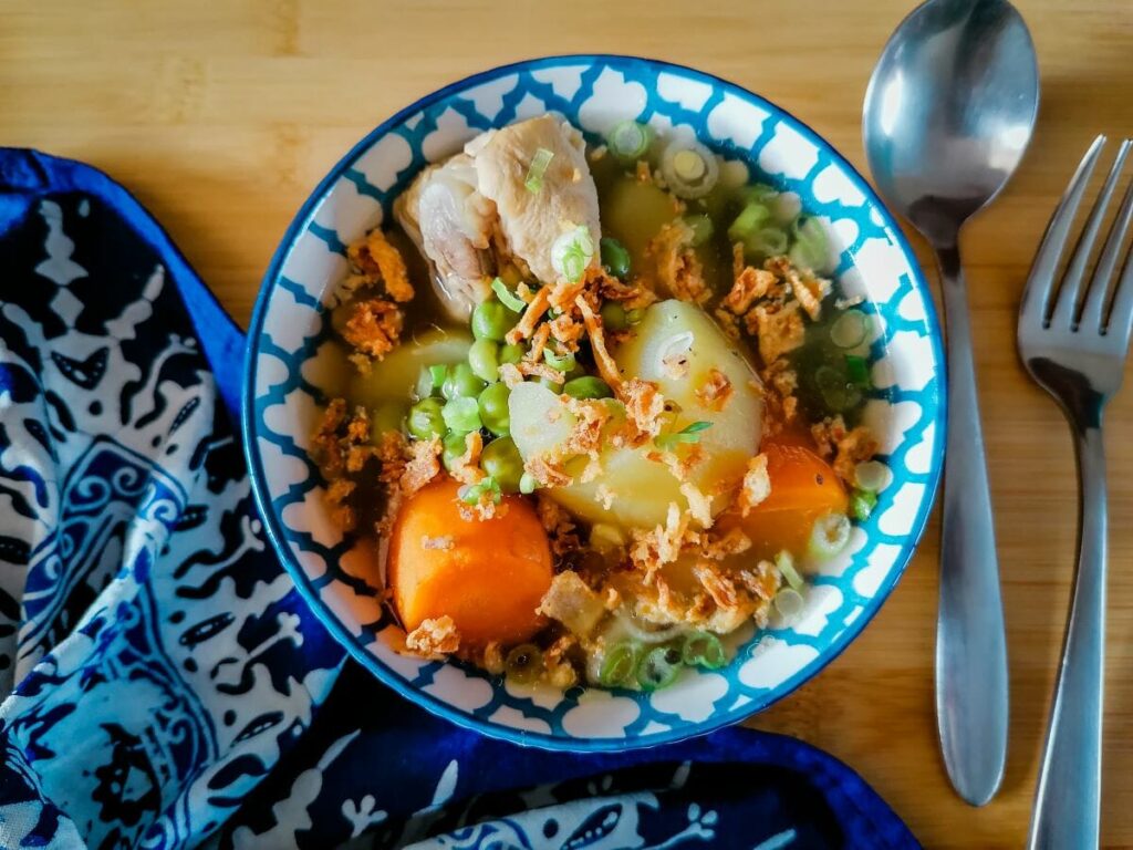 a bowl of chicken and vegetables soup with spoon and fork at the side