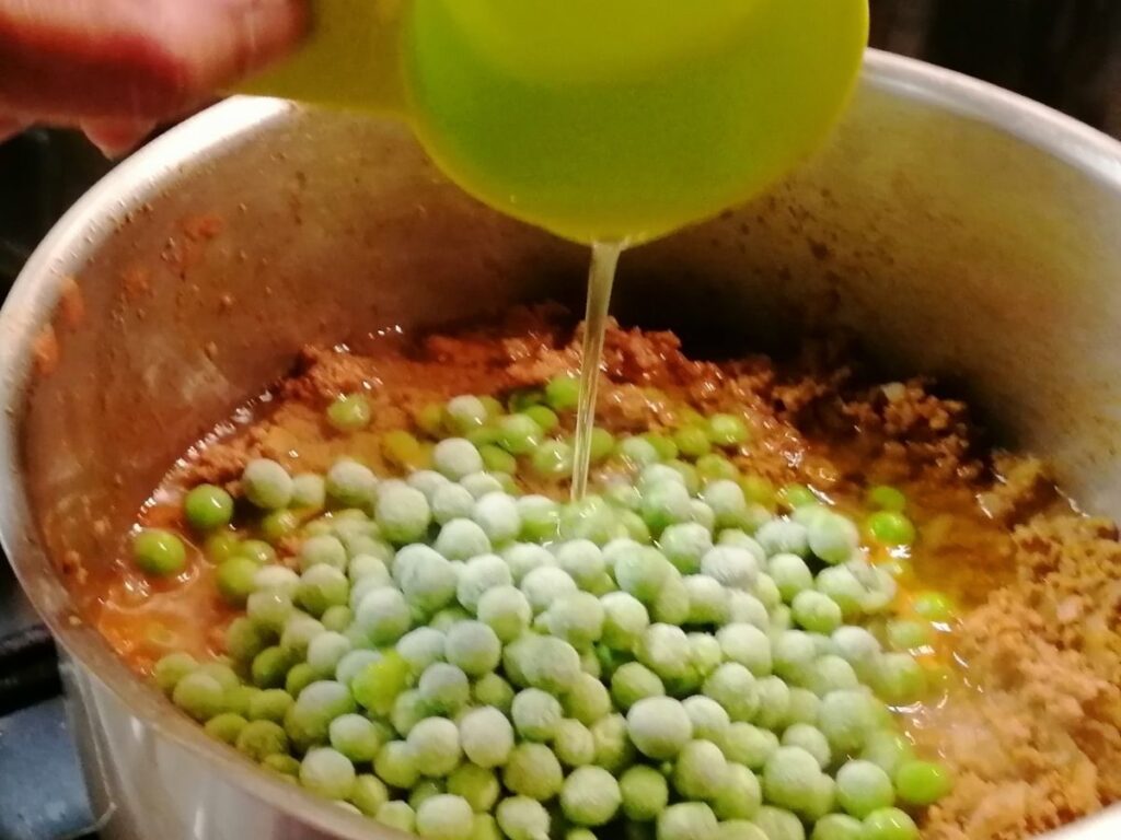 adding oil in the minced meat and green peas