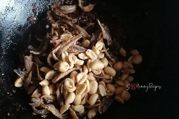 adding the fried anchovies and roasted peanuts in a wok of chilli mixture
