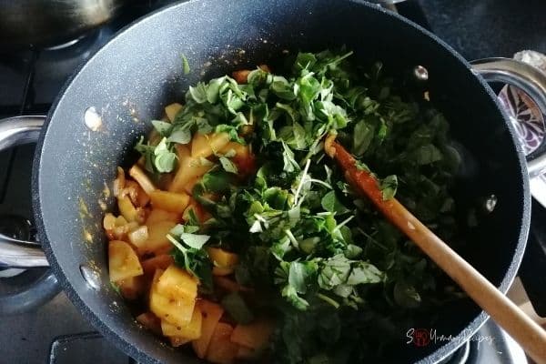 adding fenugreek leaves into potato curry