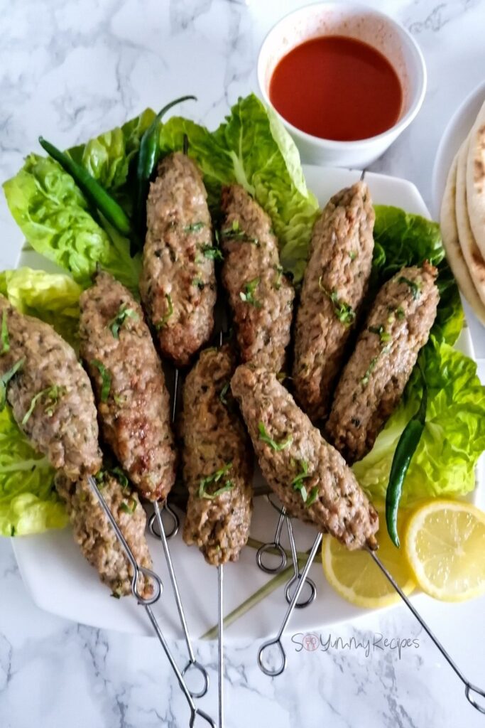 Pakistani chicken seekh kebabs with lettuces, a bowl of chilli sauce and a few slices of lemon