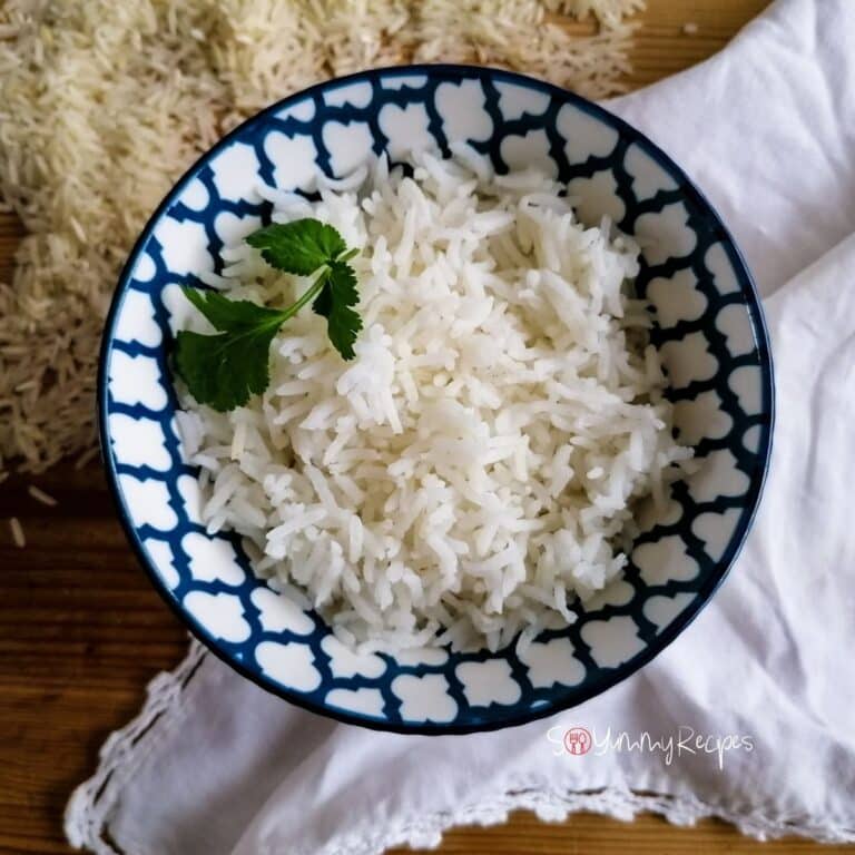 a bowl of basmati rice garnished with coriander leaves with a white napkin under the bowl and some raw rice grains near the bowl