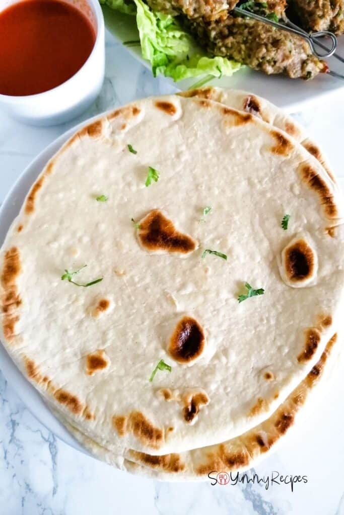 naan bread with a small bowl of chilli sauce and a plate of kebabs next to it