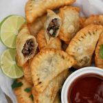 Middle-eastern samosas with a bowl of dipping sauce and slices of lime.