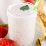 a glass of strawberry smoothie with a few strawberries around it.