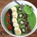 a bowl of matcha smoothie with slices of kiwi, bananas and some pecan nuts