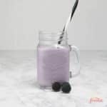 a mason jar of blueberry smoothie with a few blueberries.