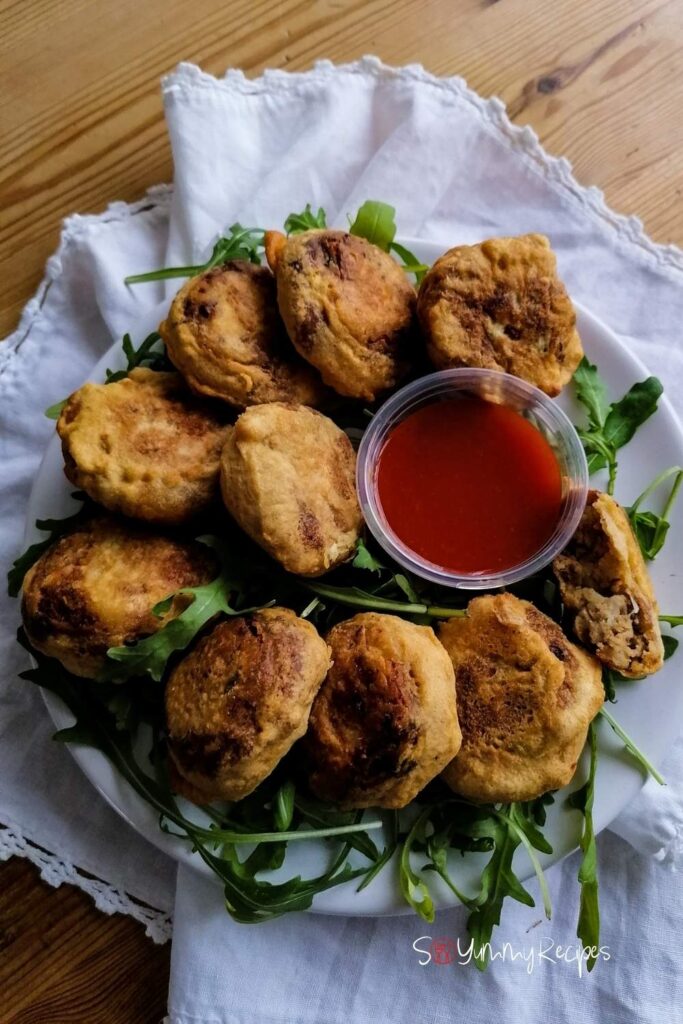 A plate of Pakistani Aloo Tikki with a small bowl of chilli sauce and some rocket leaves.
