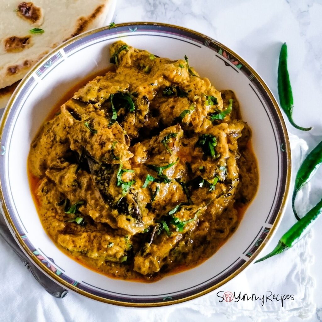 a round dish of Dahi Baingan the aubergine in spicy yoghurt sauce cooked in Pakistani style with some green chillies and naan bread around the dish