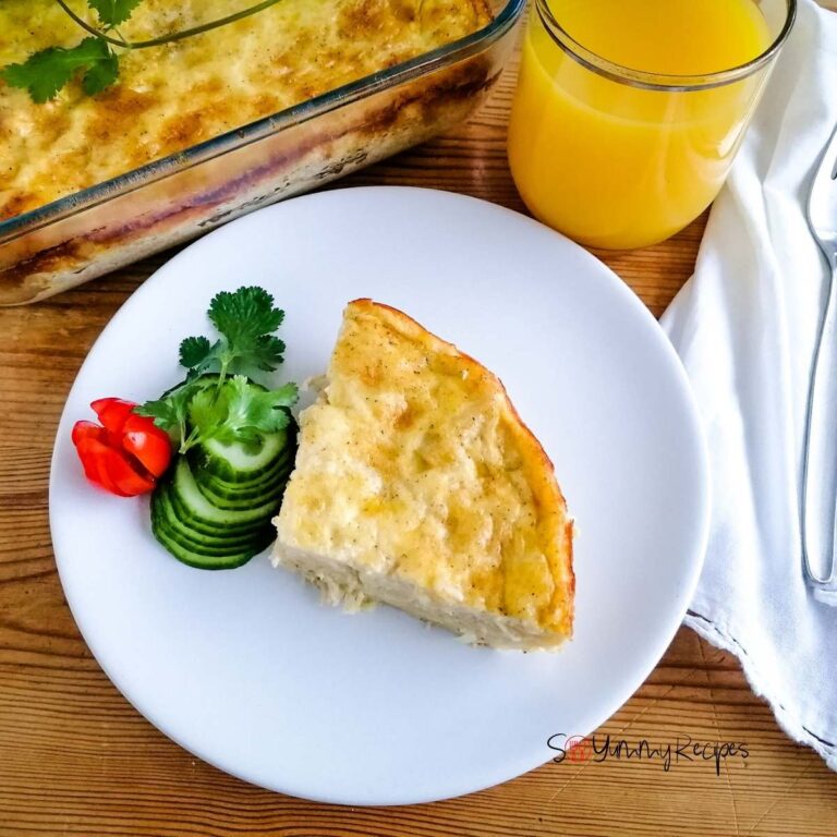 a slice of macaroni schotel with slices of cucumber and a plum tomato on a white plate with a glass of orange juice next to it