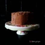 chocolate cake with chocolate mousse frosting on a white cake stand with black tile background