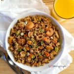 A bowl of Indonesian Nasi Goreng Seafood Recipe with a glass of orange juice and white napkin