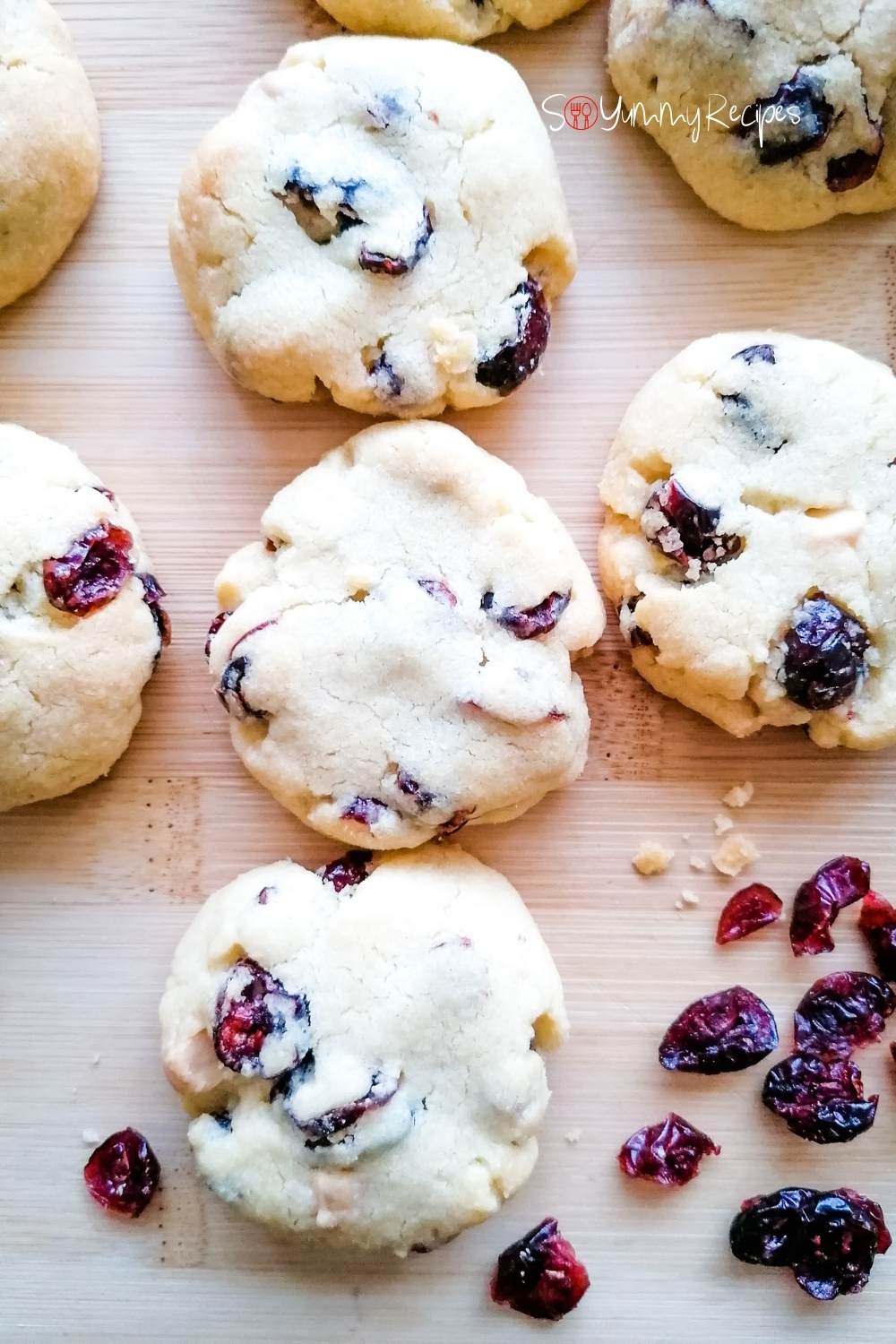 white chocolate chip and cranberries cookies with some dried cranberries on a wooden chopping board
