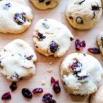 white chocolate chip and cranberries cookies on a wooden board with some dried cranberries surround them