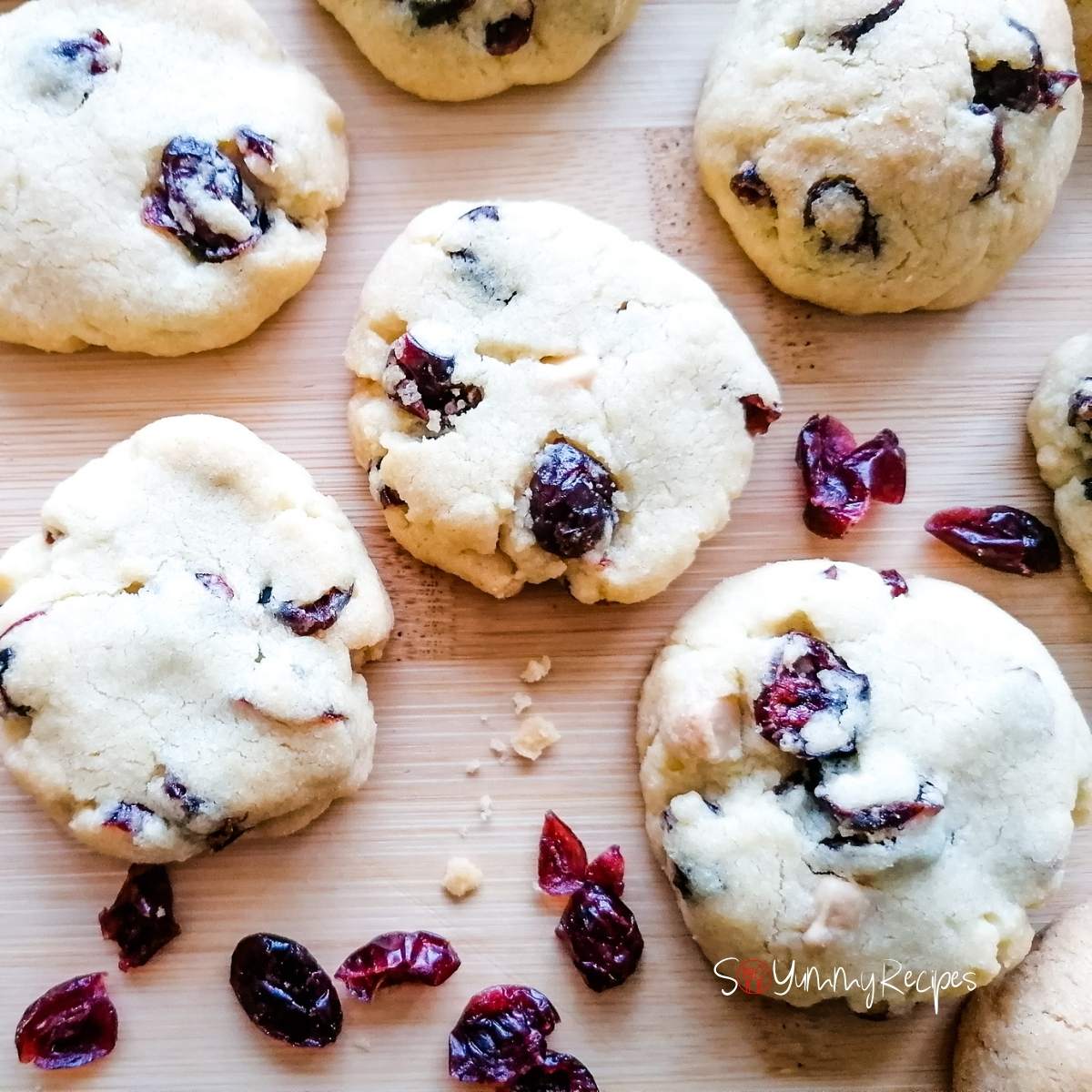 white chocolate chip and cranberries cookies on a wooden board with some dried cranberries surround them