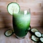 a glass of cucumber and kale smoothie with some cucumber slices around
