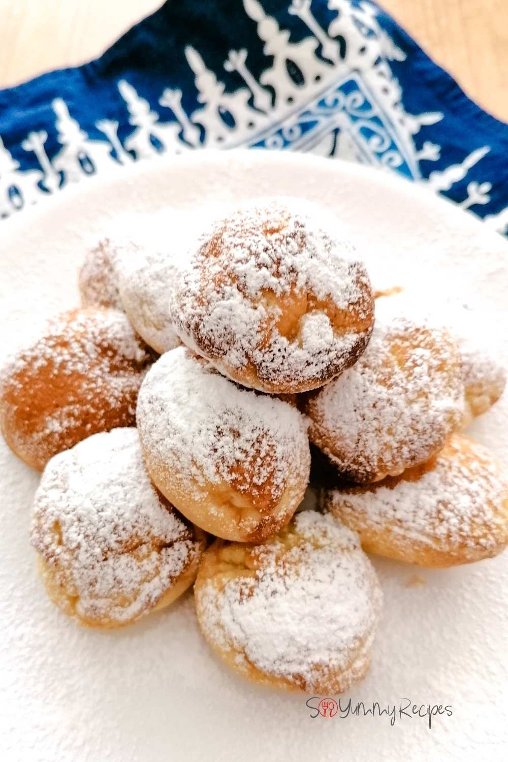 A stack of Poffertjes - the Dutch mini pancakes on a white plate with blue patterned napkin