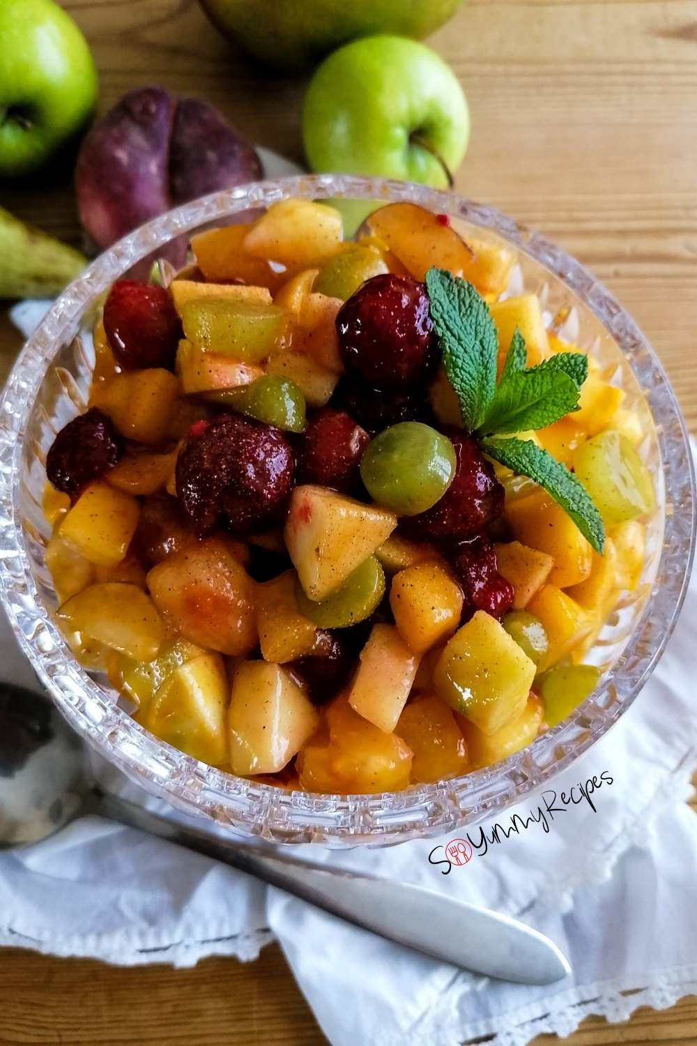 a bowl of Pakistani fruit chaat with a white napkin underneath the bowl and some fruits in the background