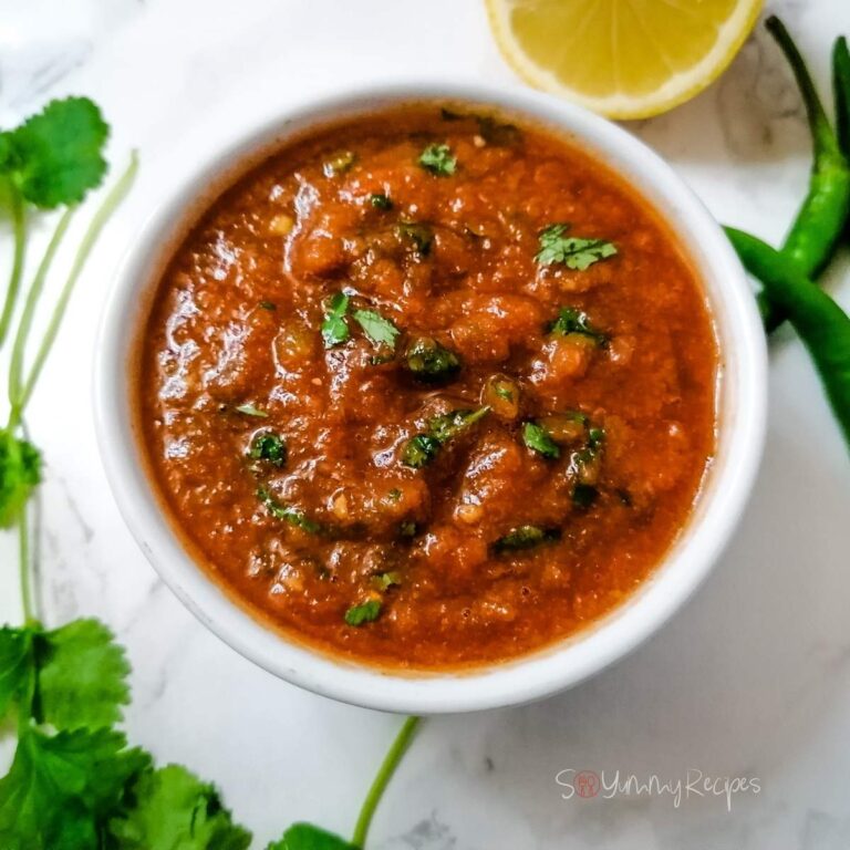 Pakistani tomato and chilli chutney in a white bowl with some coriander leaves, lemon and green chillies on the background