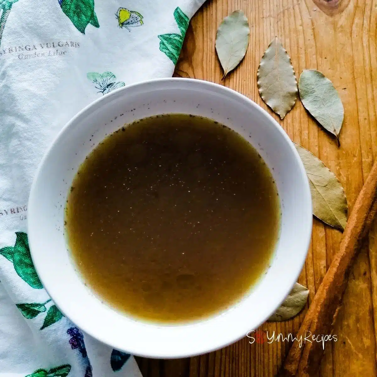 Pakistani mutton Yakhni soup in a white bowl with some bay leaves, cinnamon quill and patterned napkin.
