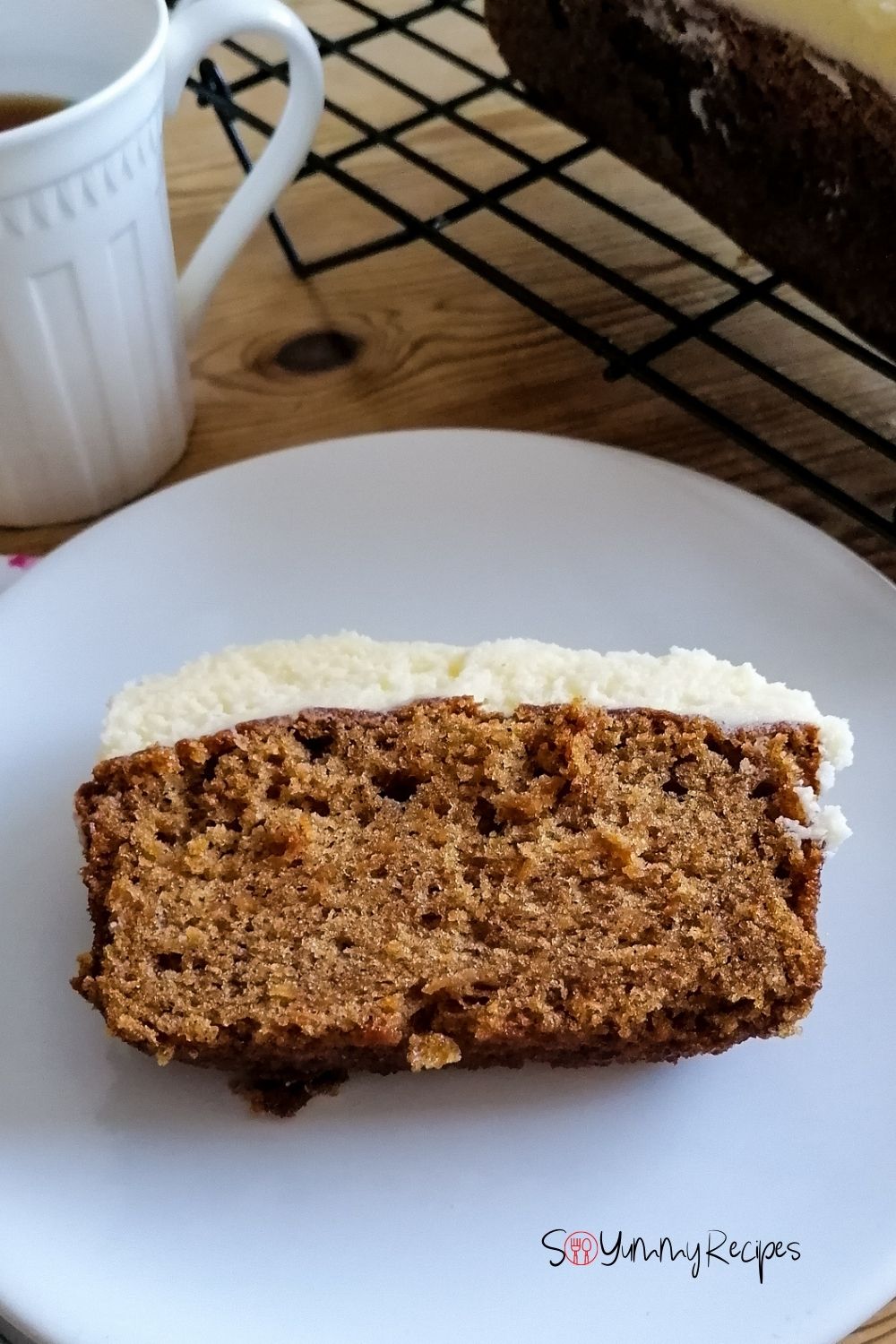 a slice of carrot cake on a white plate with a white mug on the side