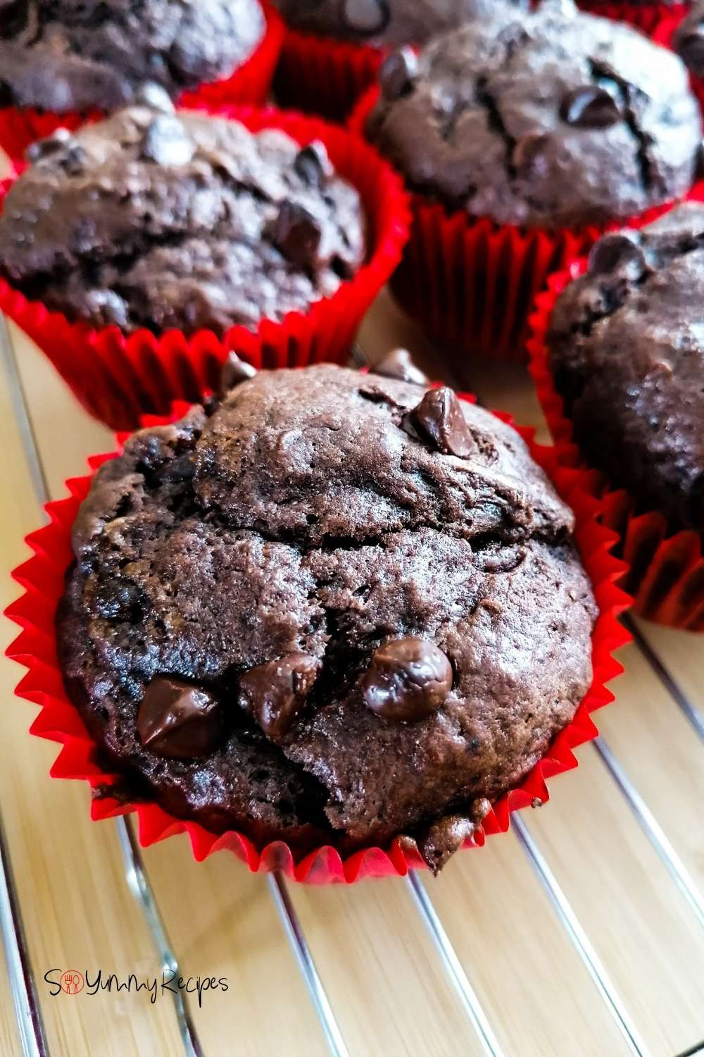 Double chocolate chip muffins in red paper cases on a cooling rack.