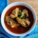 Indonesian chicken curry - Kari Ayam in a round white bowl with blue tea towel half way around the bowl.