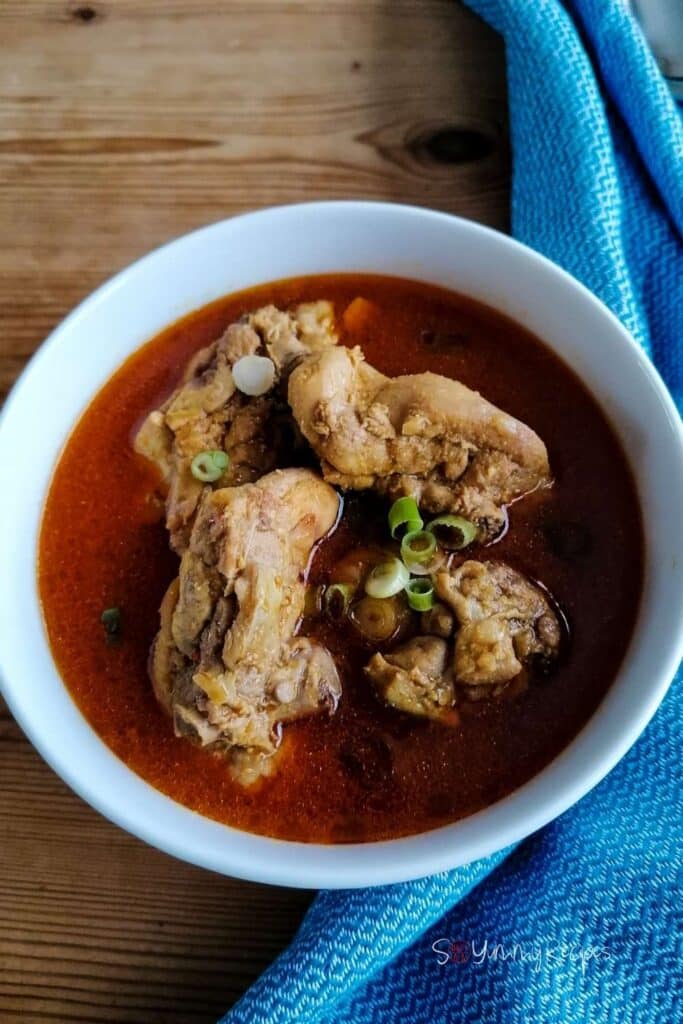 A bowl of Kari Ayam - the Indonesian chicken curry on a wooden table with blue tea towel on the right side.
