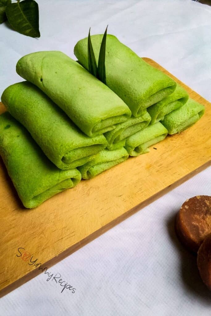 A pile of green rolled pancakes on a wooden chopping board.