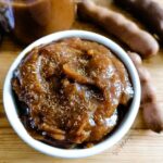 Imli sauce in a round white bowl with some fresh tamarind on the background.