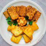 Tempe and tahu bacem on a round white plate garnished with tomato and parsley leaves.