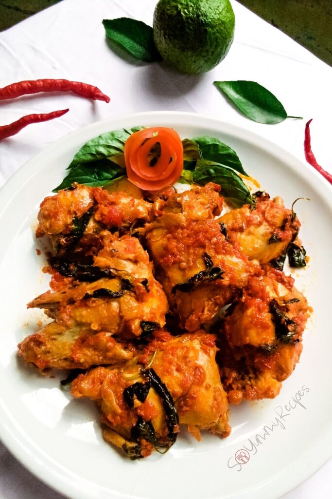 A plate of chicken dish cooked in spicy chillies with tomato and lemon basil as garnish.