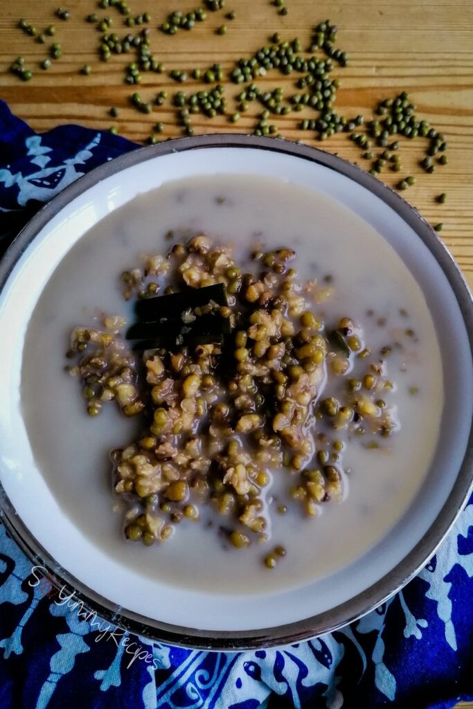 A bowl of Bubur Kacang Hijau - Indonesian mung bean dessert in palm sugar and coconut milk with blue pattern napkin and some dried mung beans as the background.