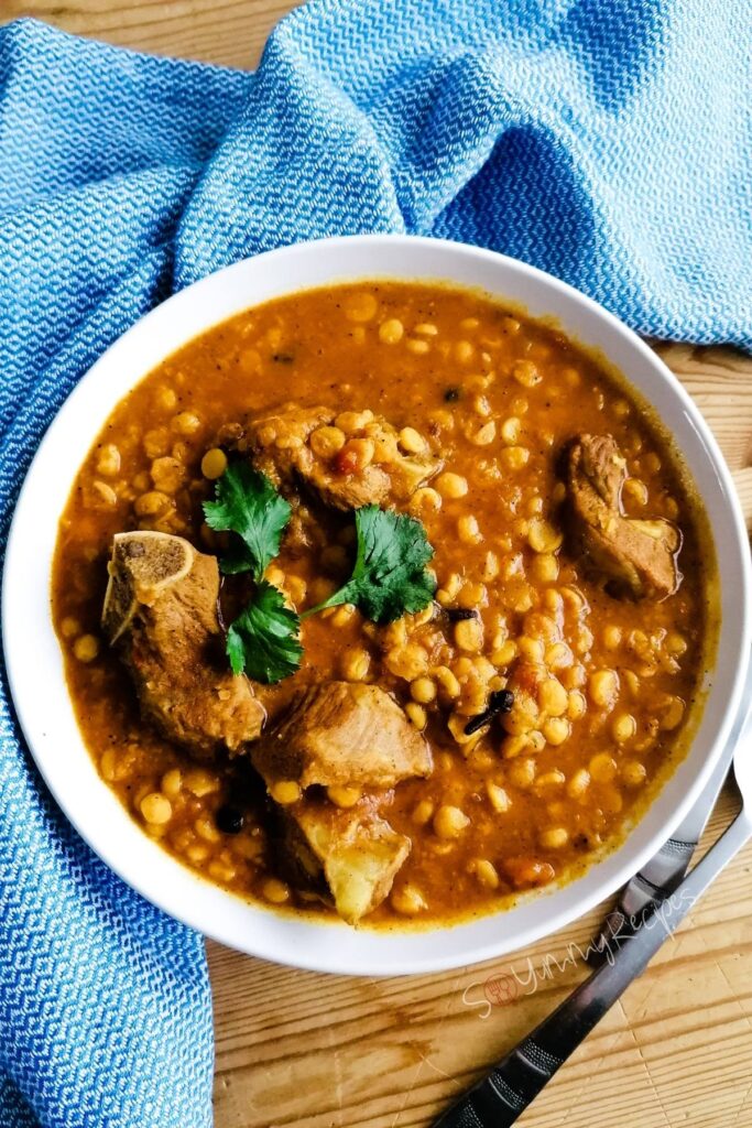 A bowl of Dal Gosht - the Pakistani lentil and meat curry - garnished with coriander leaves with blue patterned napkin and cutlery on the background.