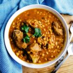Dal Gosht the lentil and meat curry in a white bowl with blue patterned napkin and cutlery on the background.