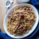 An oval dish of Lamb pilau rice with a blue napkin on the background.