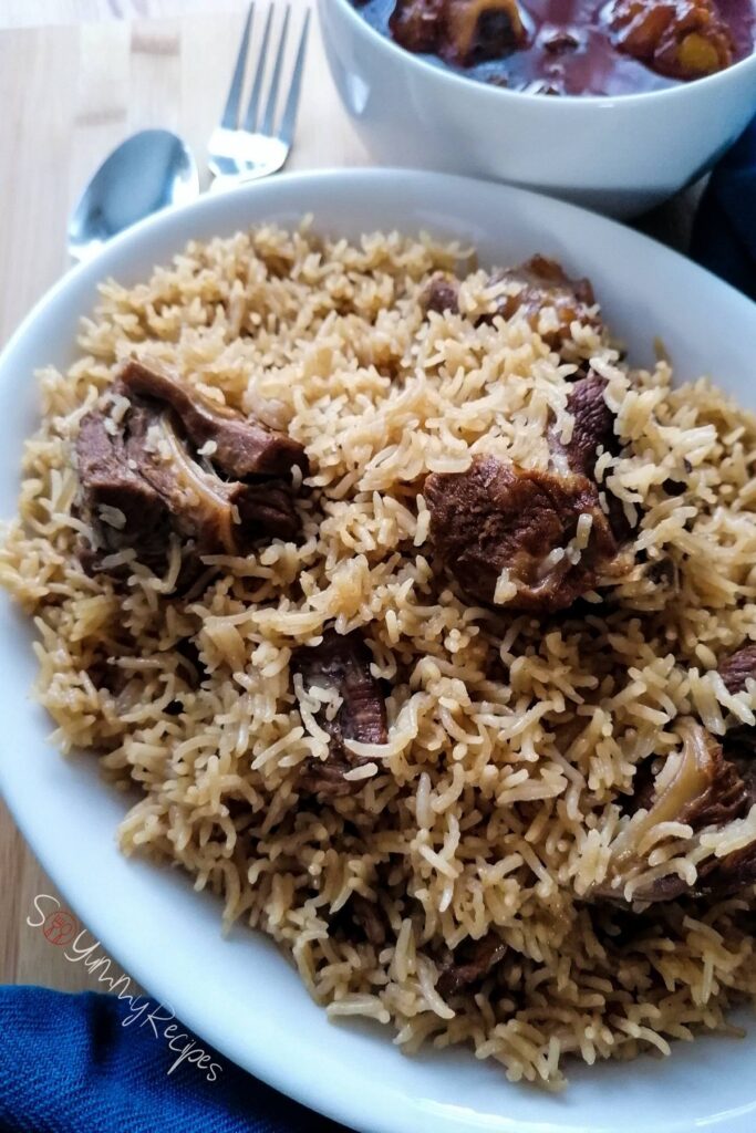 Lamb pilau rice in an oval white dish with spoon and fork next to it.