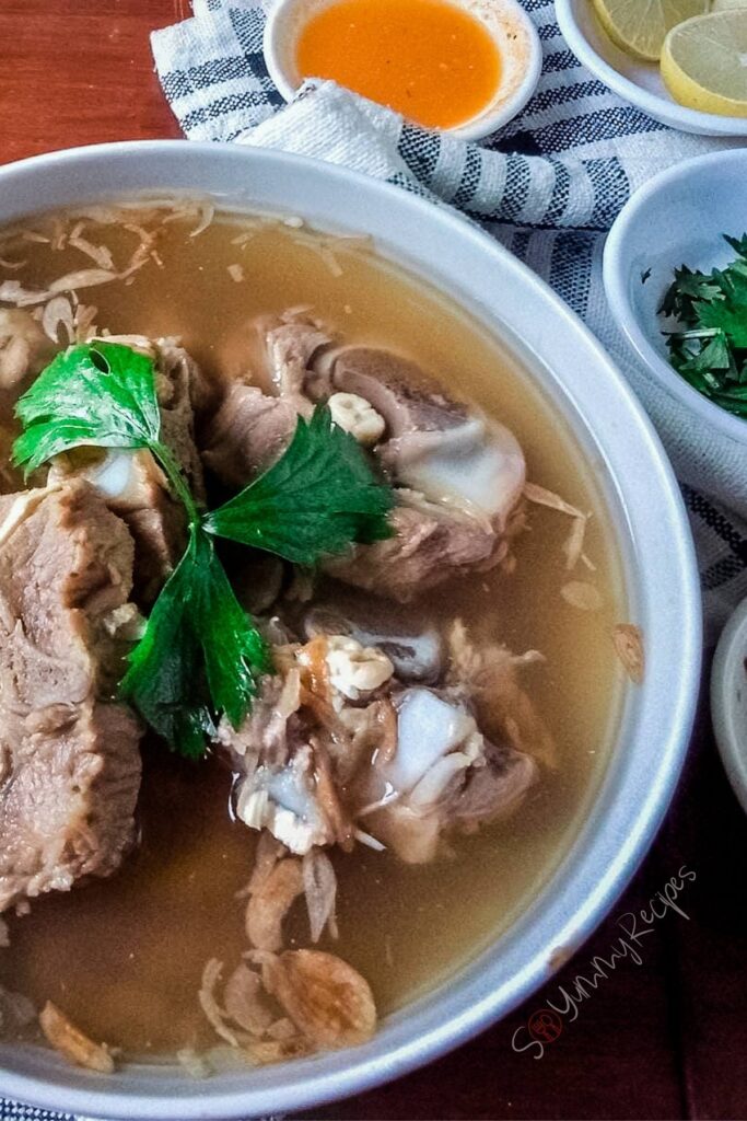 Sop Buntut the Indonesian oxtail soup with some small bowls containing chilli sauce, lemon slices and chopped parsley.
