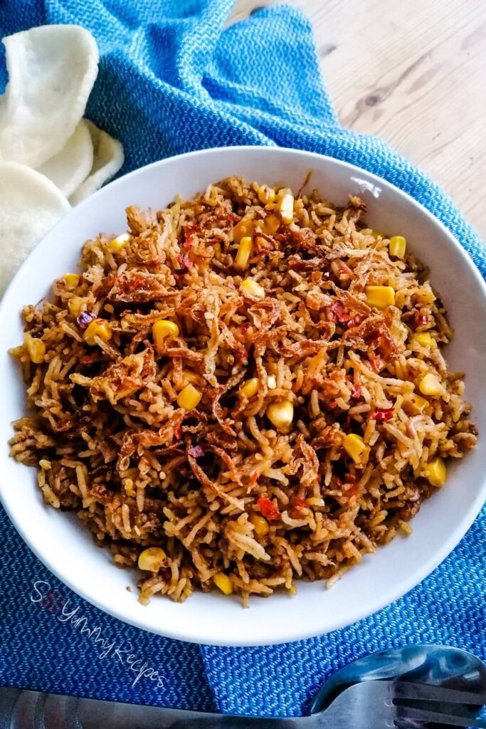 A deep plate of Indonesian tuna fried rice - nasi goreng tuna - with some prawn crackers on the side and blue napkin on the background.