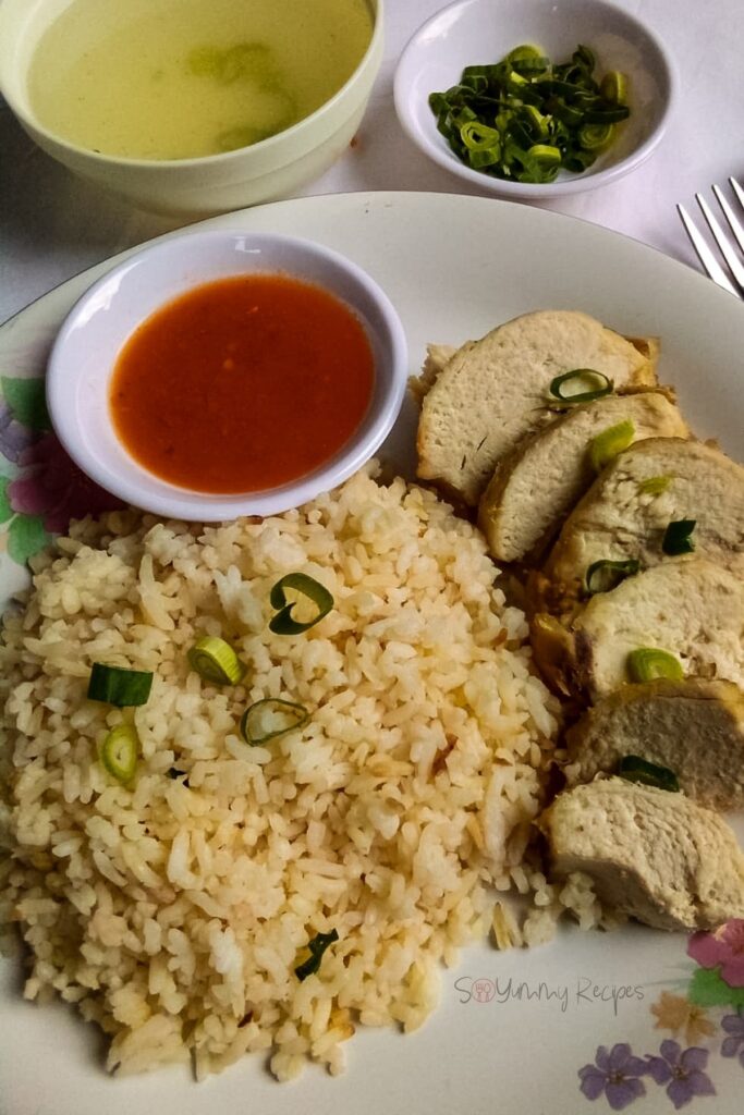 Nasi Ayam Hainan with a bowl of soup, chilli sauce and spring onion slices in a small bowl.