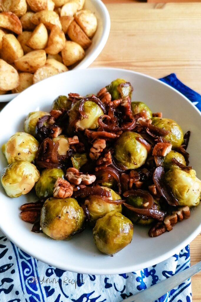 roasted brussels sprouts with honey on a round shallow bowl with roast potatoes on the background.