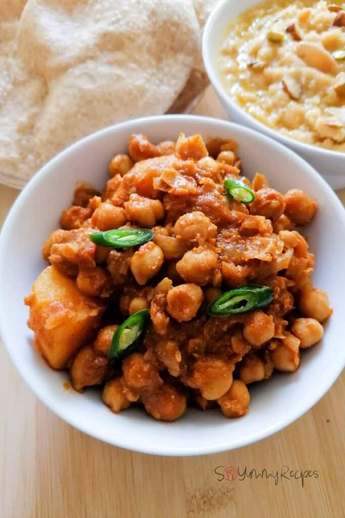 A bowl of chickpea and potato curry garnished with sliced green chillies.