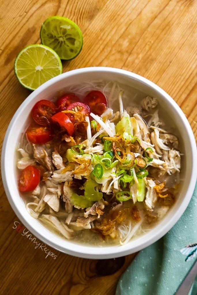 Indonesian chicken noodle soup in a bowl with lime and napkin in the background.