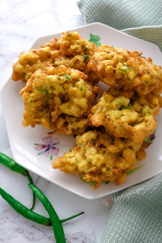 corn fritters on a white plate with green chillies next to it.