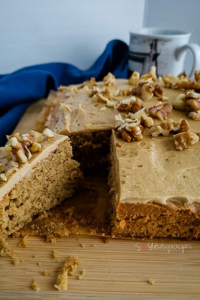 Sliced coffee and walnut cake tray bake with dark blue napkin in the background.