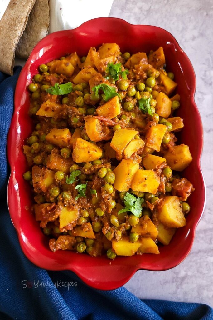 Potato and green pea curry in a red rectangle dish.