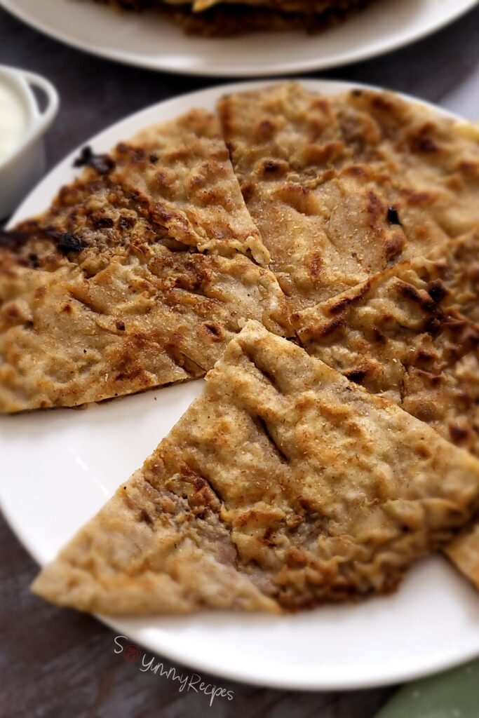 Pakistani keema paratha cut in pieces on white plate.